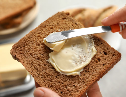 Espatula com manteiga sendo passada numa fatia de pão.
