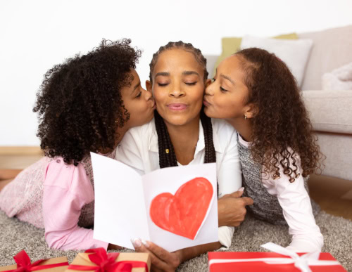 Ideias de presente no Dia das Mães: escolhas úteis e cheias de afeto 1 Duas filhas beijando a mãe nas bochechas.