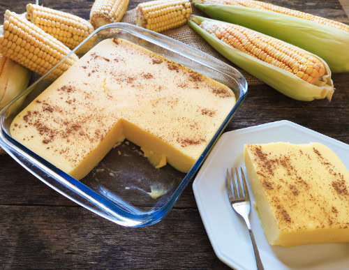 Canjica nordestina: tradição e sabor das festas juninas 1 Travessa com canjica e fatia num prato branco com garfo ao lado.