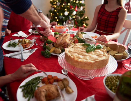 Ceia de Natal simples: preparação, receitas e dicas para sua festa 1 Pessoa fatiando frango em mesa de ceia de Natal.