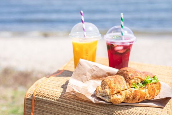 O que levar para comer na praia: ideias práticas e econômicas 9 Dois copos de sucos e sanduíche na praia.